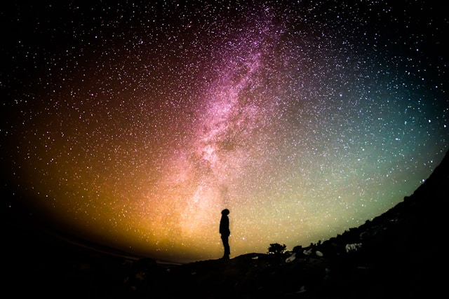 What is Spiritual Ascension Silhouette of a person standing under a vibrant, star-filled night sky with a colorful Milky Way stretching across the horizon.