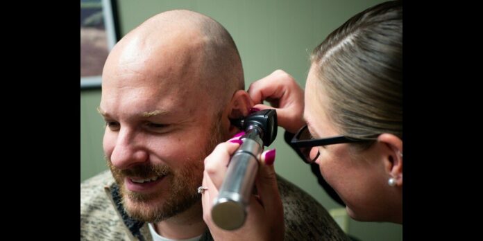 Doctor examines a smiling man's ear with an otoscope during checkup Doctor examines a smiling man's ear with an otoscope during checkup