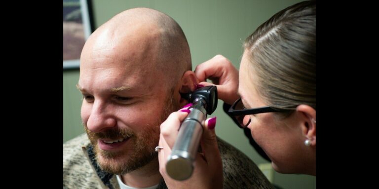 Doctor examines a smiling man's ear with an otoscope during checkup