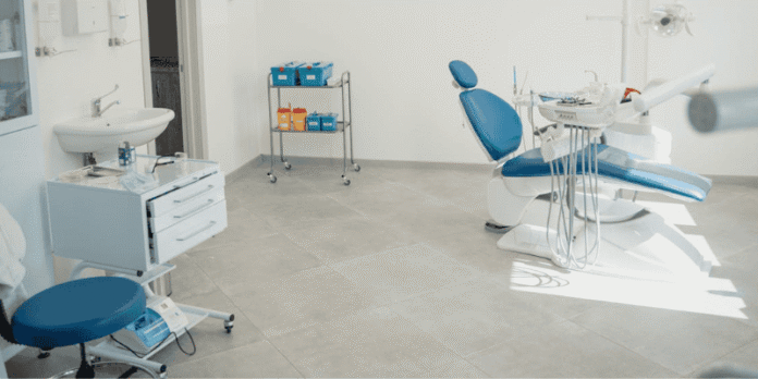 Modern dental clinic room with blue patient chair and clean equipment setup.