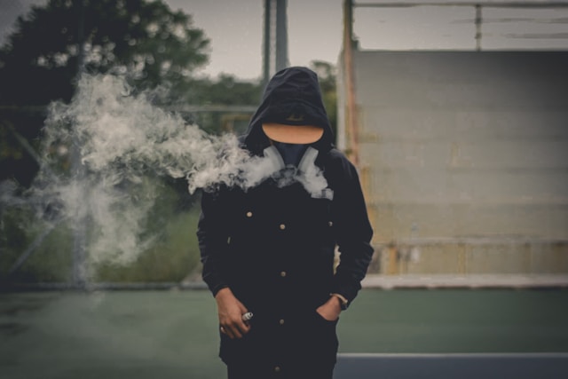 Person wearing a hooded jacket exhaling smoke outdoors, representing lifestyle habits linked to health risks