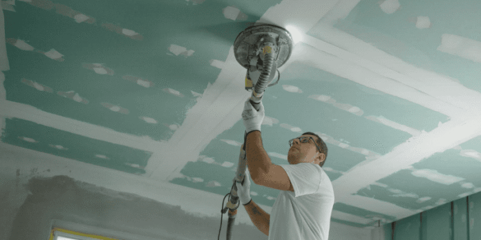 Renovator sanding drywall ceiling during interior renovation.