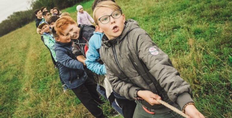 Children participating in a tug-of-war game during summer camp programs on a grassy field