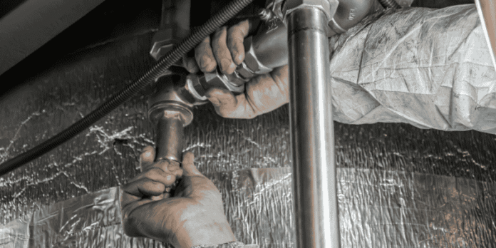 Plumber Repairing Metal Pipes Underneath a Sink Plumber Repairing Metal Pipes Underneath a Sink