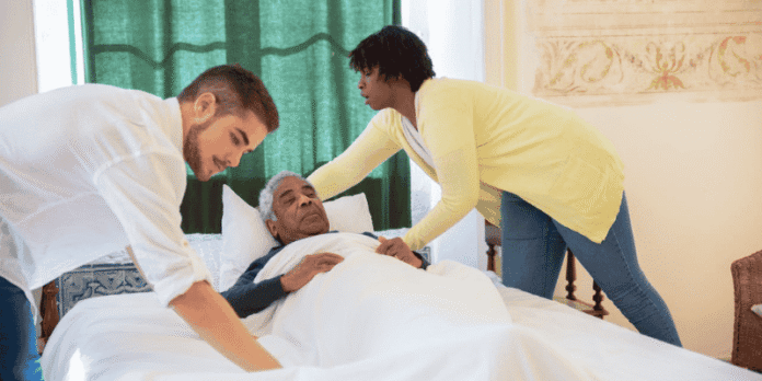 Two caregivers assist an elderly man lying in bed
