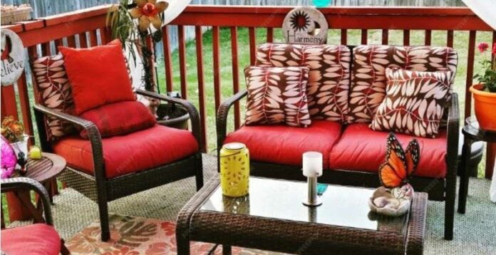 A cozy patio setup with wicker furniture, red cushions, a glass table, and plants, showing how patio furniture creates an inviting outdoor retreat.