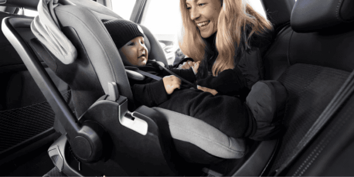 smiling mother interacting with her baby who is securely seated in a rear facing car seat inside a car
