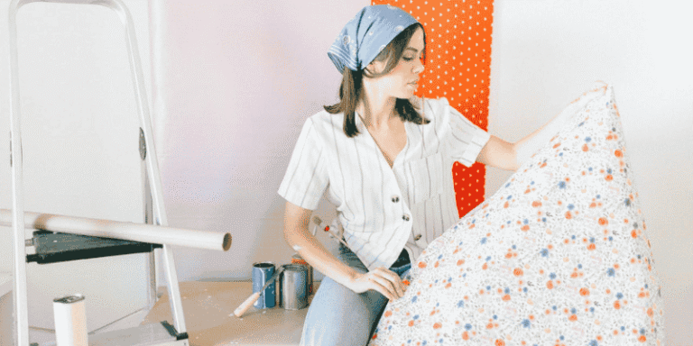 Woman holding decorative wallpaper while preparing for home improvement project with paint cans and ladder in the background
