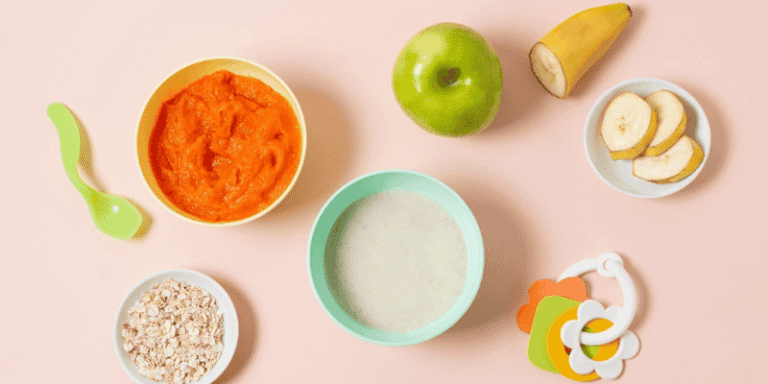 A flat lay of baby food items including pureed carrots, banana slices, apple, and oatmeal on a pastel background.