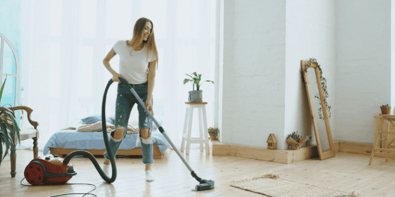 Woman vacuuming a bright, tidy bedroom to improve home cleaning efficiency and maintain a fresh living space.