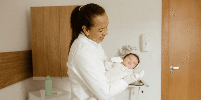 A midwife holds and smiles at a newborn baby in a hospital setting, symbolizing hands-on learning during a midwifery internship.