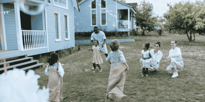 Parents supervising kids playing games in a grassy yard near houses, representing a safe and tidy outdoor play area.