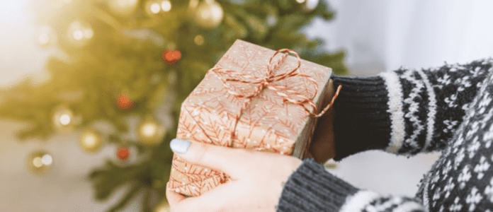 A person in a winter sweater holds a wrapped Christmas gift