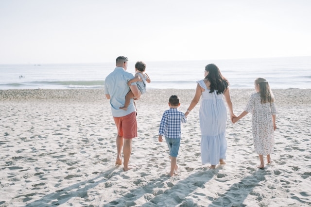 A family walking hand in hand along a sunny beach, capturing a fun-filled vacation that keeps parents and children happy together.