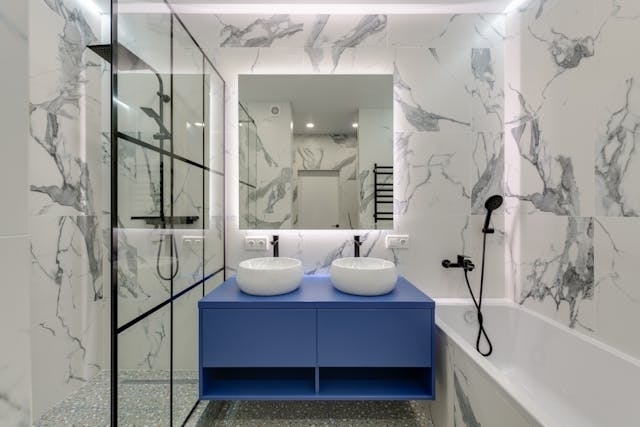 Design Considerations Before Updating Your Bathroom A modern bathroom featuring marble walls, a glass shower, and a double sink vanity, highlighting important design choices for a bathroom update.