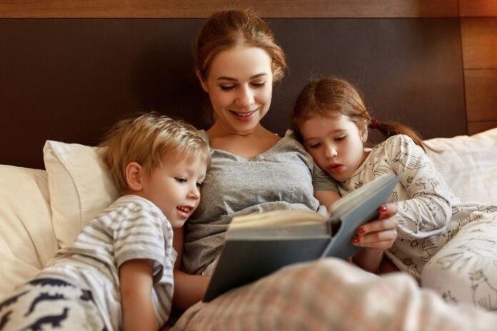 Mom and children reading a book in bed