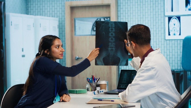 Doctor Reviewing Spine X-Ray With Patient During Consultation Doctor and patient discussing a spinal X-ray image during a medical consultation about potential spine surgery.