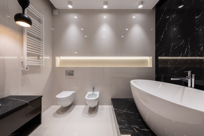 A Modern Luxury Bathroom A modern bathroom featuring a white freestanding soaking tub, sleek wall mounted fixtures, and soft ambient LED lighting against black marble accents.