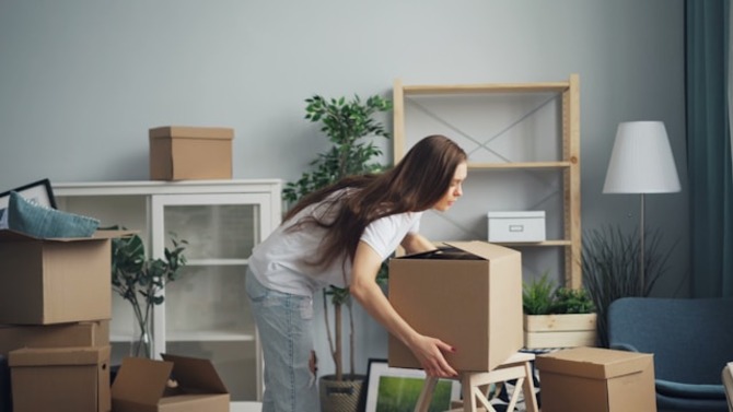 A young woman packing household items into cardboard boxes.