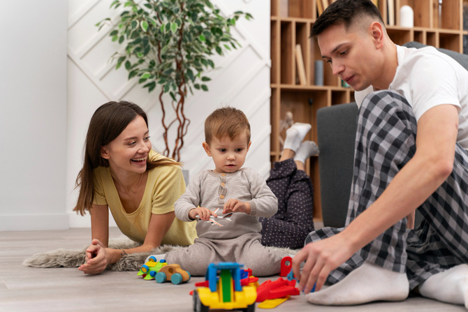 Parents Playing With Toddler Child on Living Room Floor at Safe Home Environment Mother and father sitting on the floor with their toddler child, playing with colorful toys in a bright and safe home living room environment.
