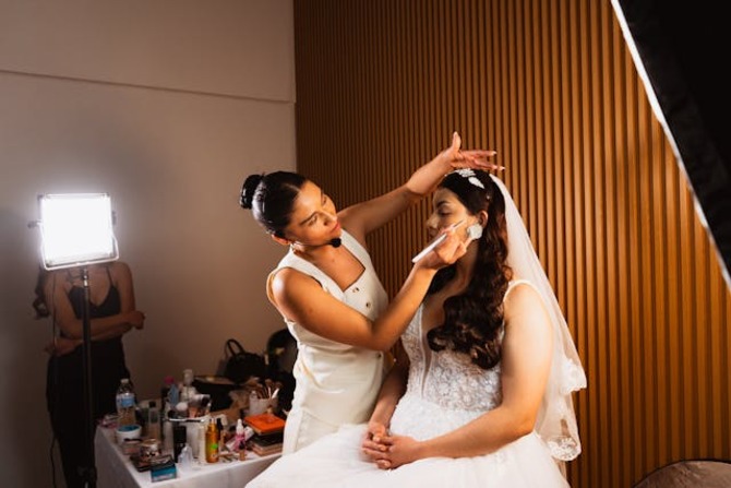Professional Makeup Artist Preparing Richmond Brides for Wedding Day A professional makeup artist carefully applies makeup to a Richmond bride wearing a white wedding gown and veil while preparing her for the wedding day in a softly lit indoor studio.